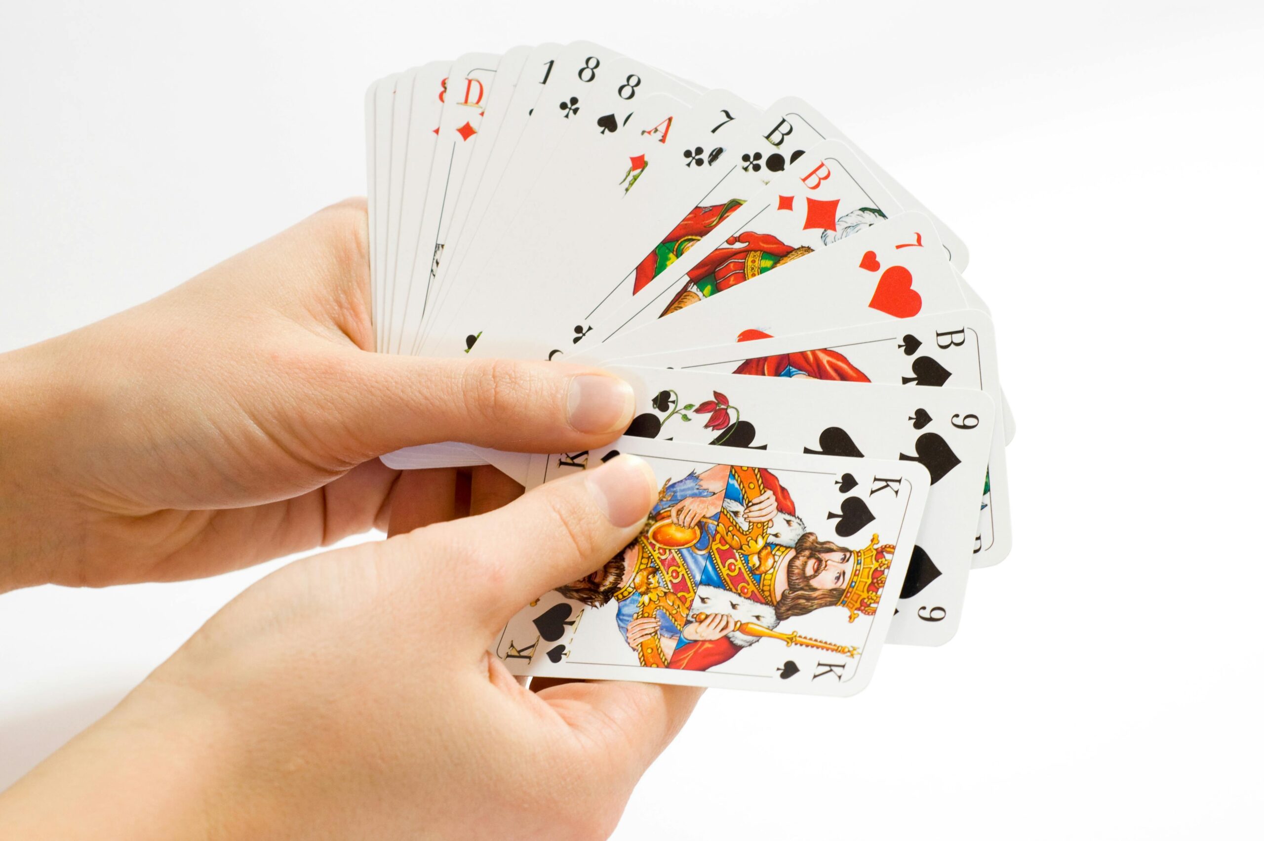 Colorful playing cards fanned out in hands against a white background.